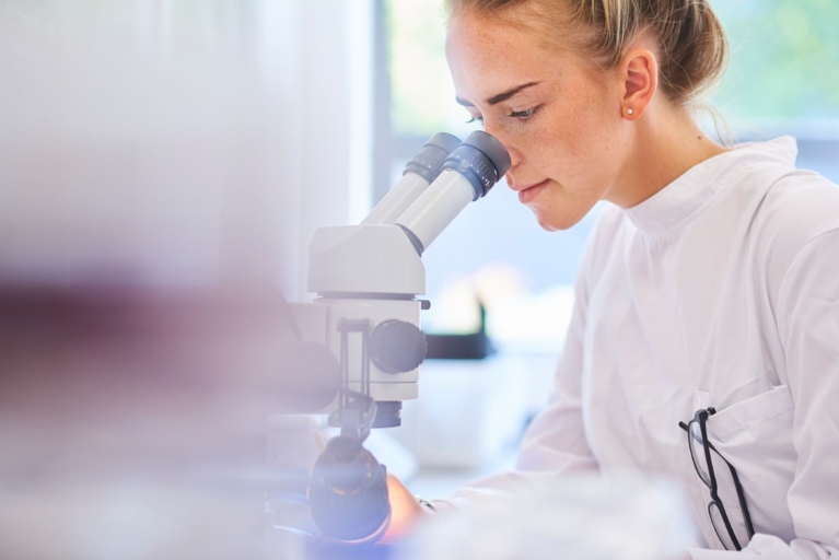 Young woman scientist looking through microscope